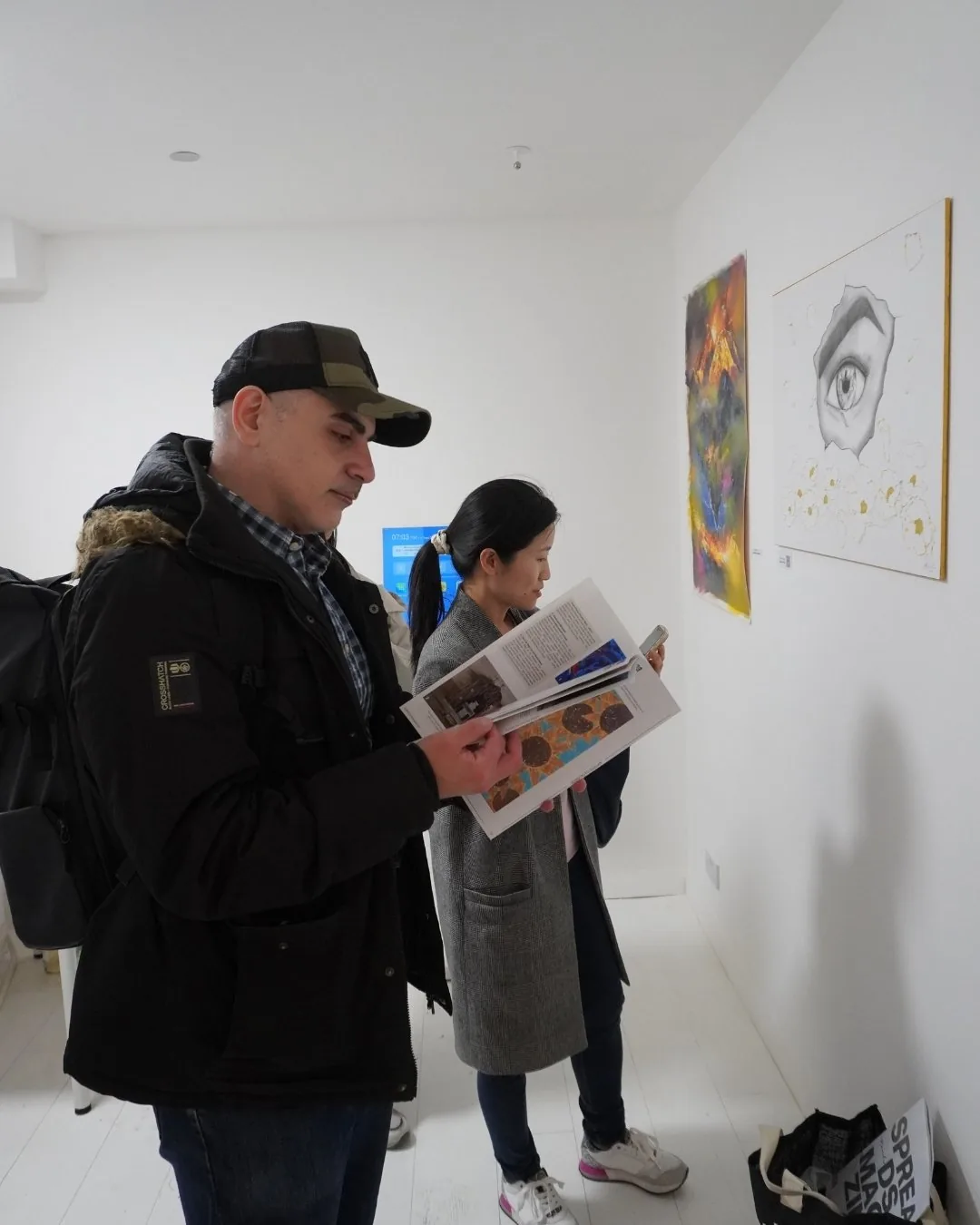 A visitor in a cap reading an open art magazine in the gallery.